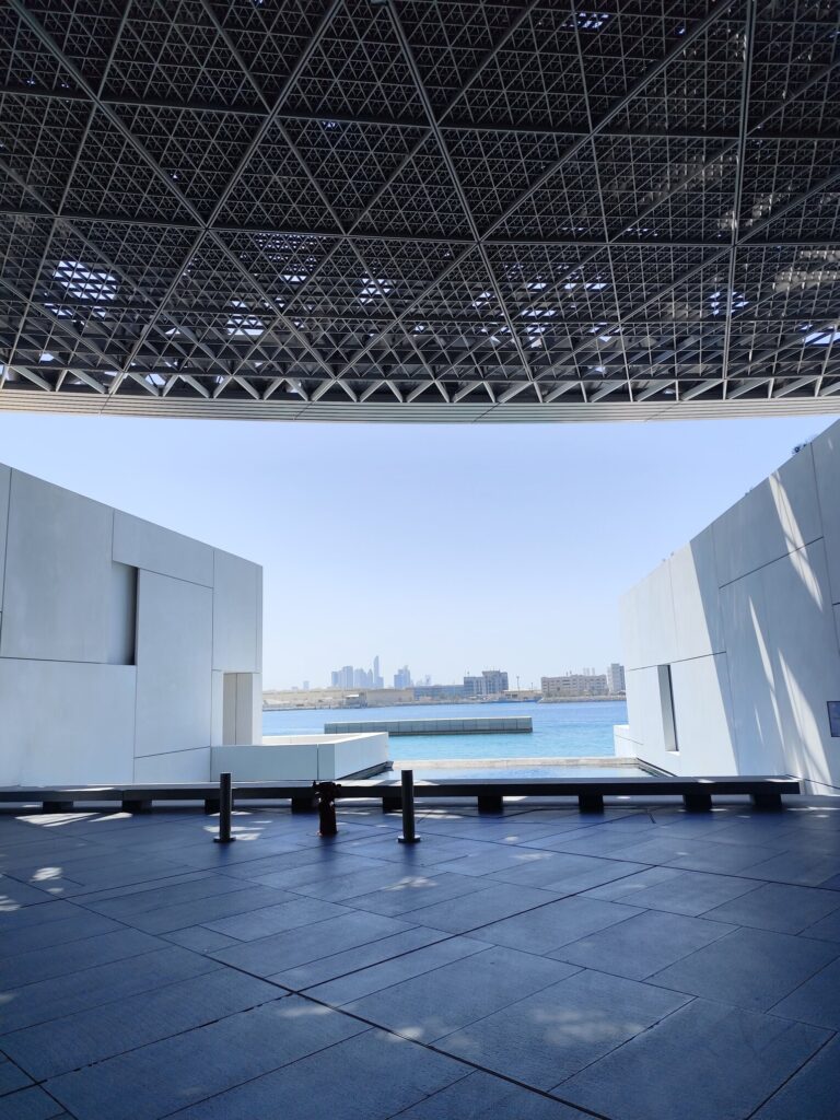 View of modern architecture at Louvre Abu Dhabi with city skyline in the background.