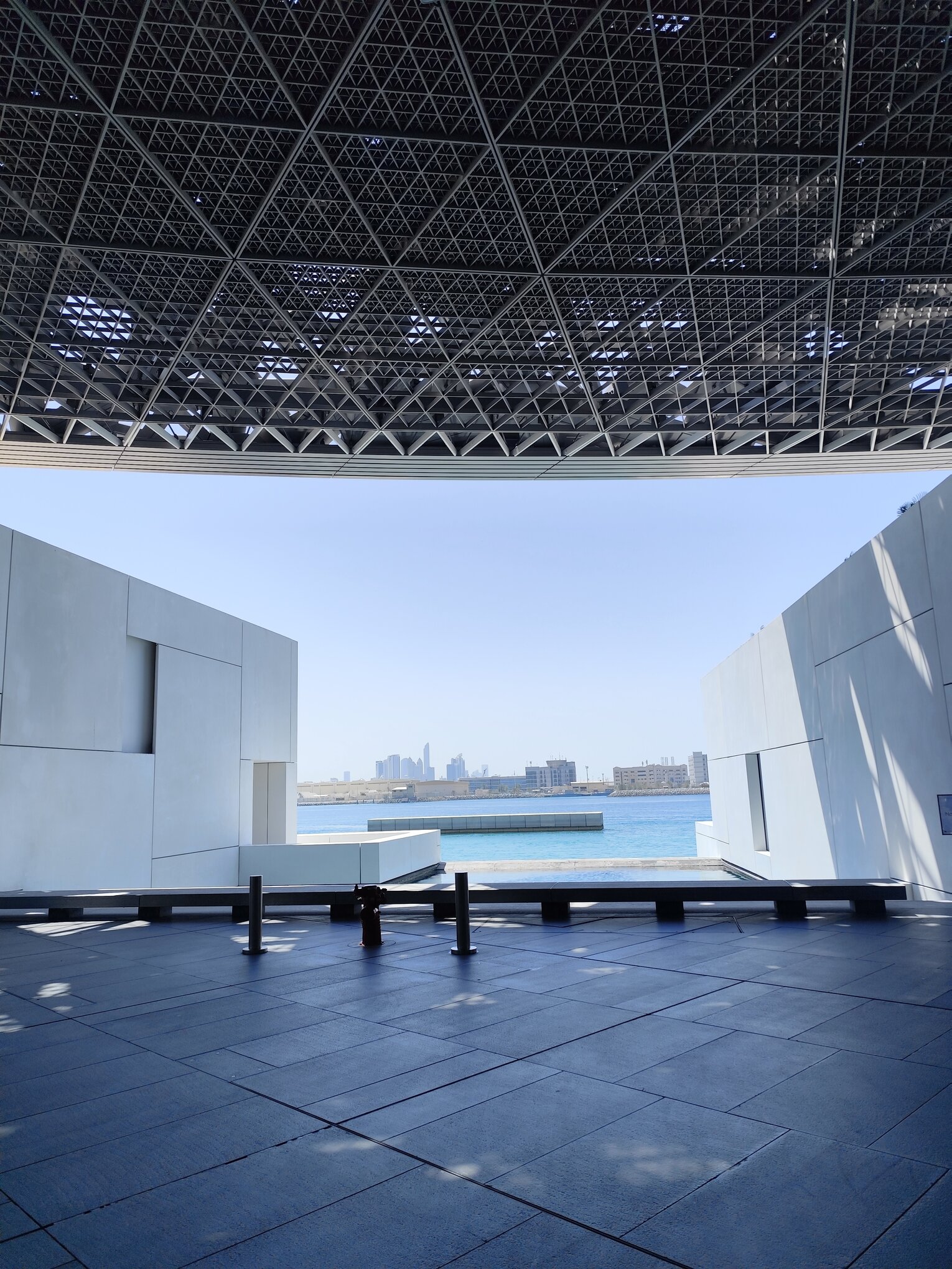 View of modern architecture at Louvre Abu Dhabi with city skyline in the background.