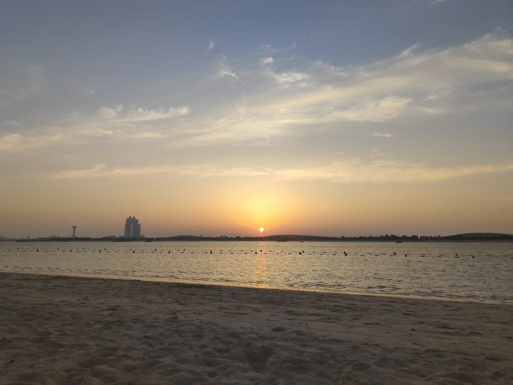 Sunset view over Abu Dhabi beach with city skyline in background.