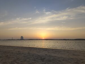 Sunset view over Abu Dhabi beach with city skyline in background.