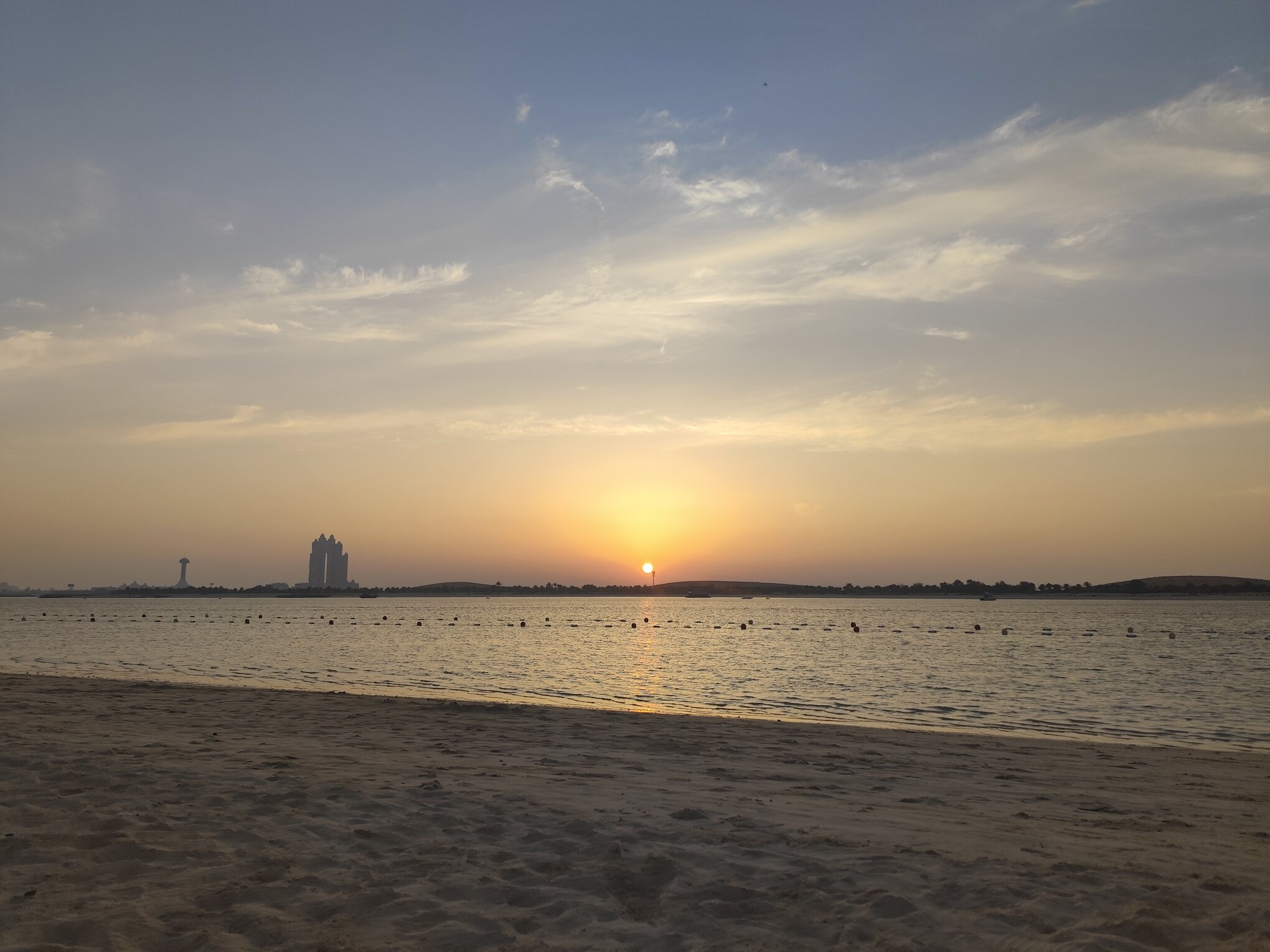 Sunset view over Abu Dhabi beach with city skyline in background.