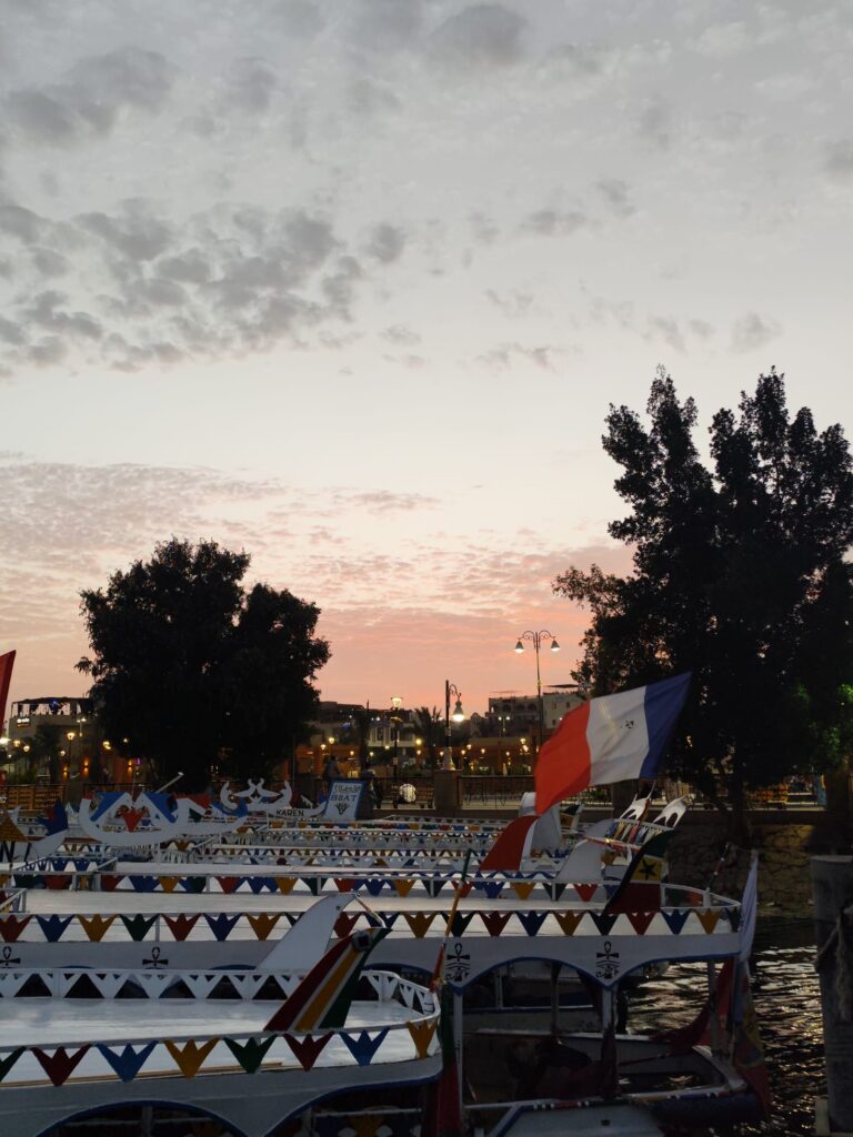Colorful feluccas on the Nile River at sunset with a flag visible.