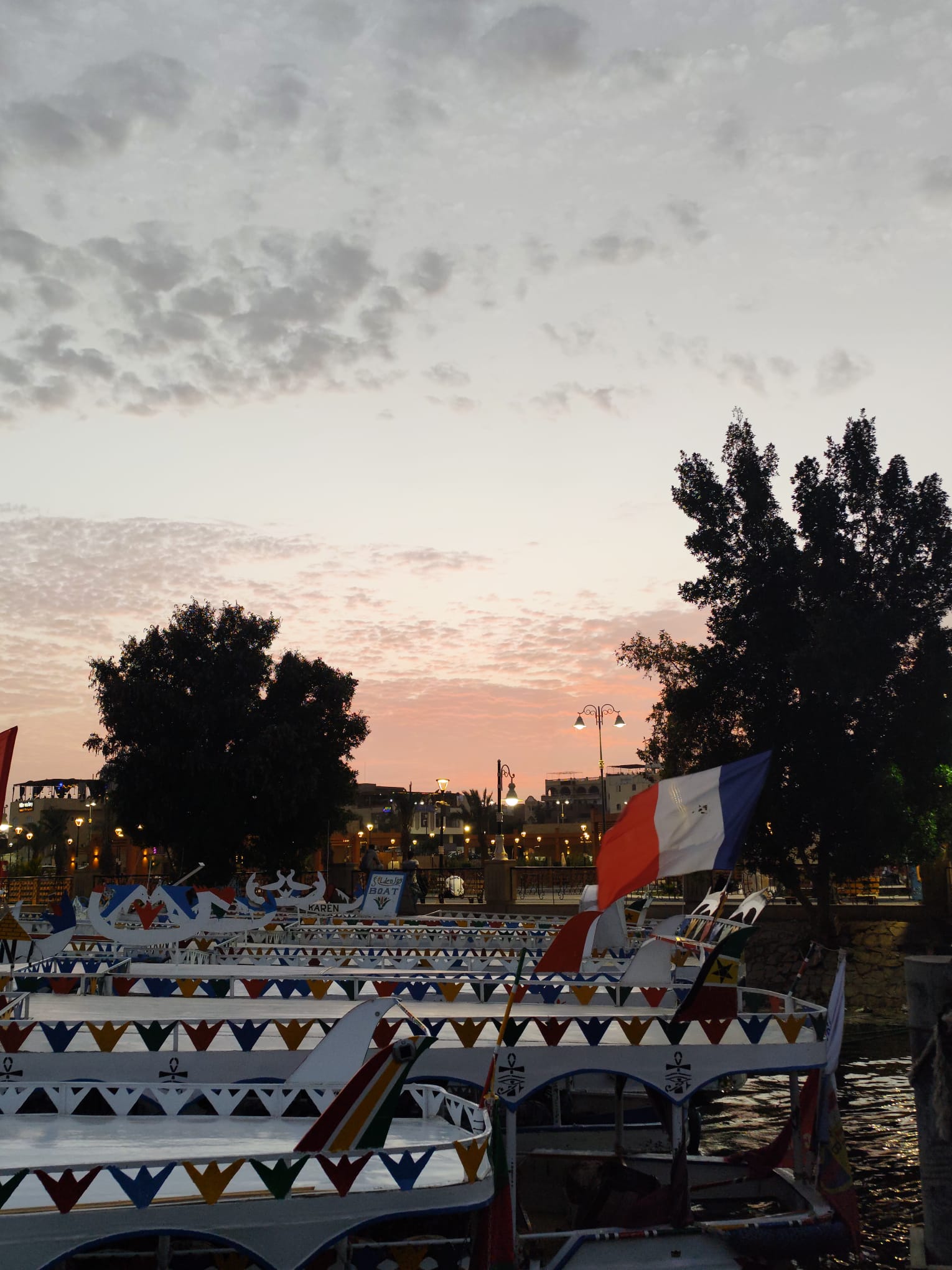 Colorful feluccas on the Nile River at sunset with a flag visible.