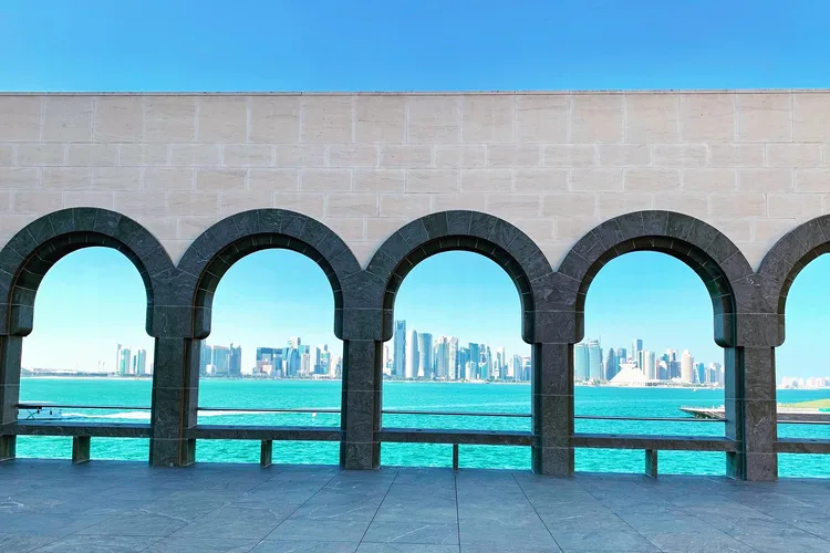 View of Doha skyline through stone arches under a clear blue sky.