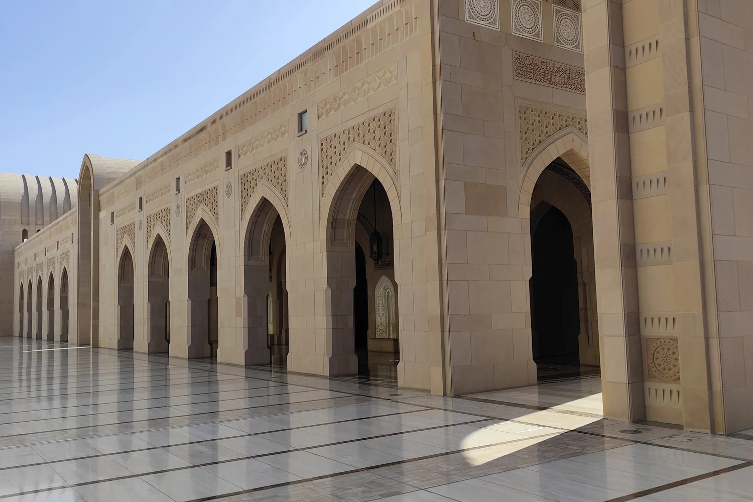 Exterior arches of the Grand Mosque in Muscat, showcasing intricate stonework.