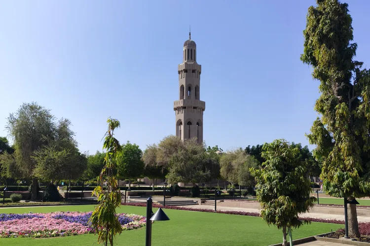 The minaret of the Grand Mosque in Muscat with surrounding gardens and trees.