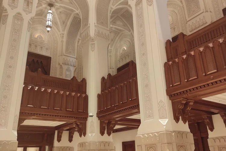 Interior view of the Grand Mosque in Muscat with ornate wood carvings and intricate ceilings.