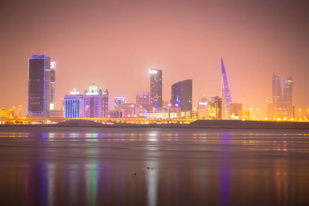 Glowing Manama skyline at night with colorful lights reflecting on water in Bahrain.