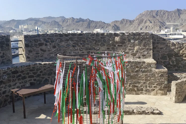 Colorful flags in Mutrah Fort courtyard against mountains in Muscat.