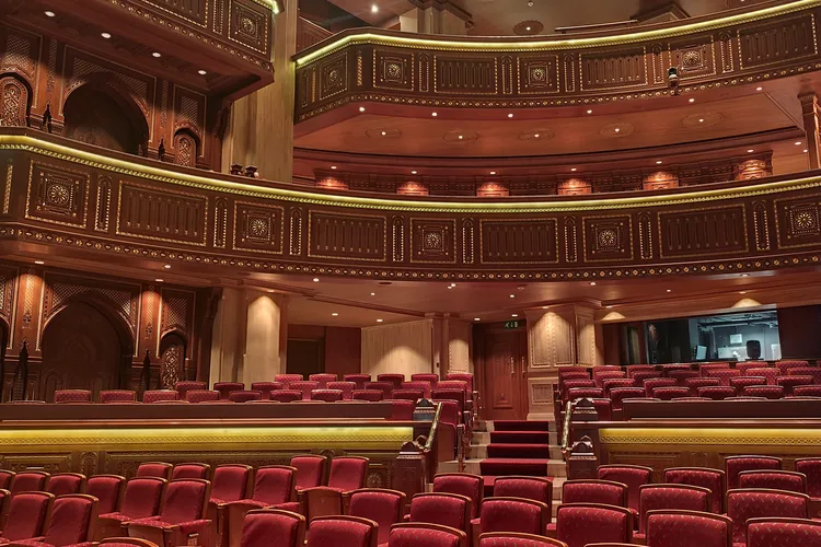 Interior of Royal Opera House Muscat with ornate wooden balconies and red seats.