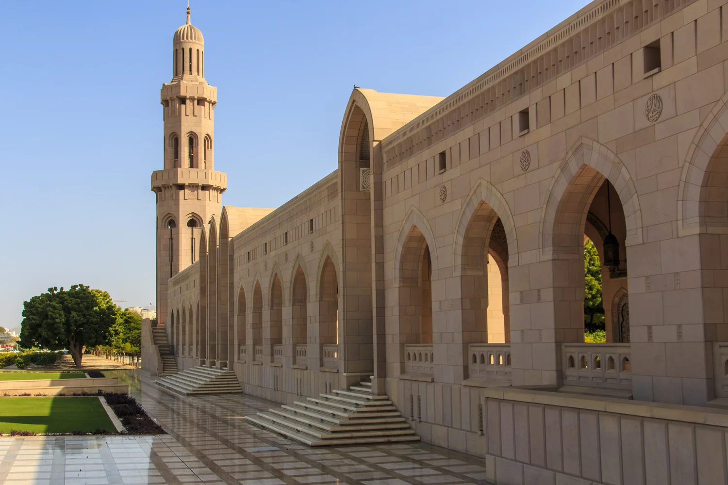 View of Sultan Qaboos Grand Mosque with elegant arches and a minaret in Muscat, Oman.