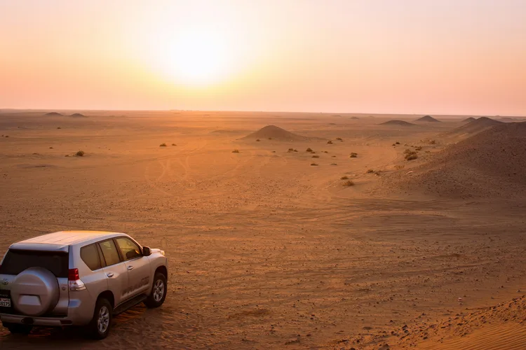 Car driving through the Kuwaiti desert at sunset with dunes visible.