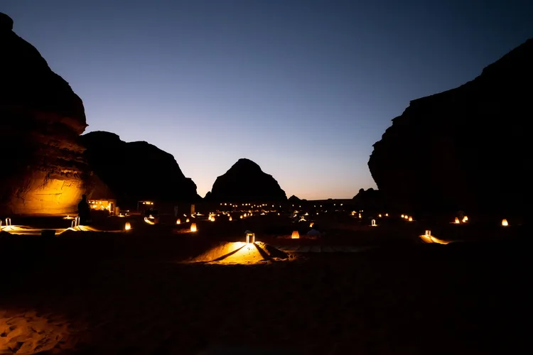 Illuminated desert setting in AlUla under a darkening sky.