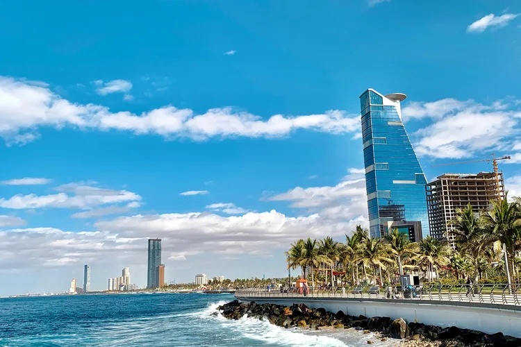 Modern buildings along the Jeddah waterfront with palm trees and a clear blue sky.