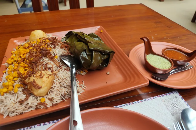 Omani Shuwa served with rice, wrapped leaves, and sauces.