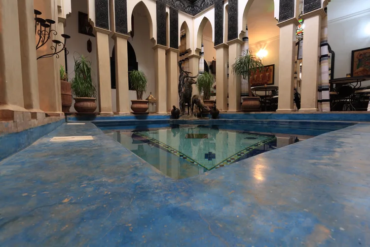 Interior of a traditional Moroccan riad with a blue-tiled pool in Marrakech.