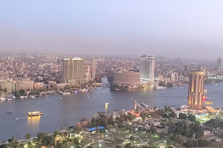 Cairo skyline with Nile River at sunset, city lights visible.